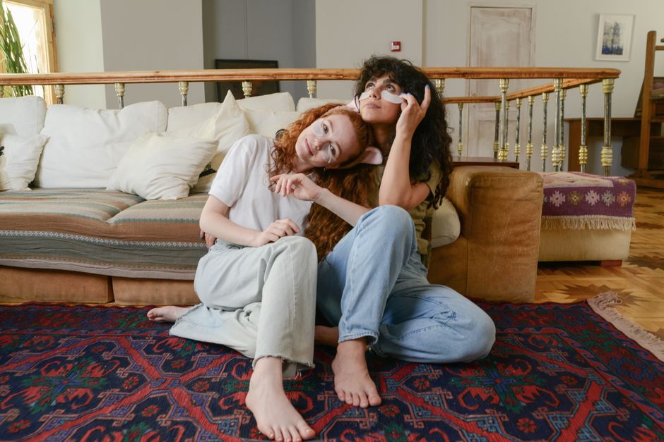 Two women sitting on a cozy carpet, enjoying a skincare routine with under eye patches.