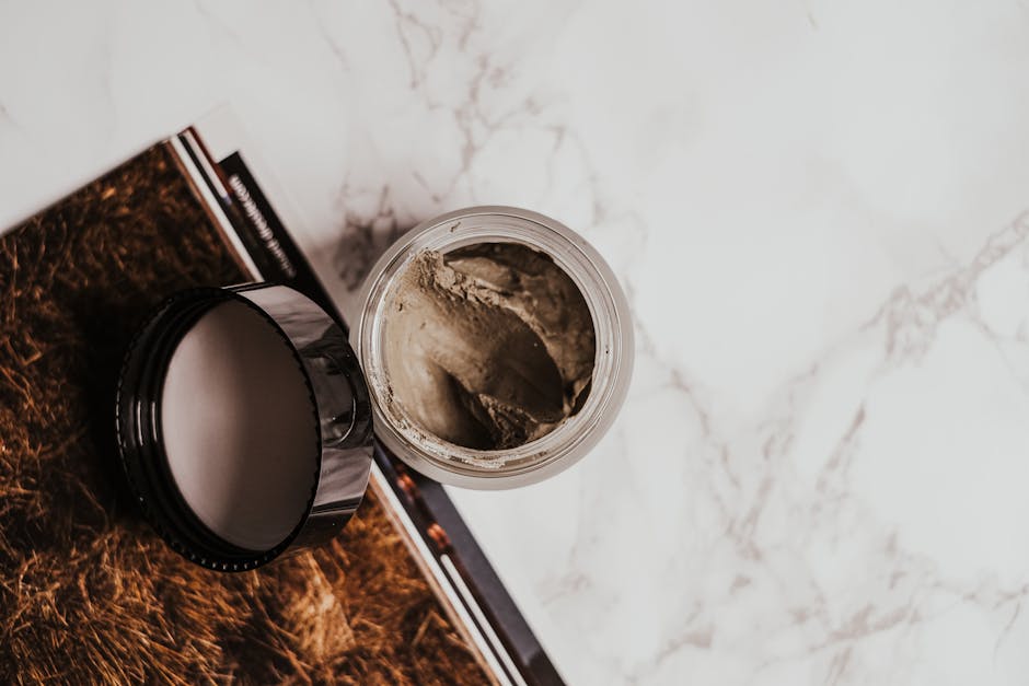 High-angle view of a clay mask in a glass jar on a marble surface with a magazine.