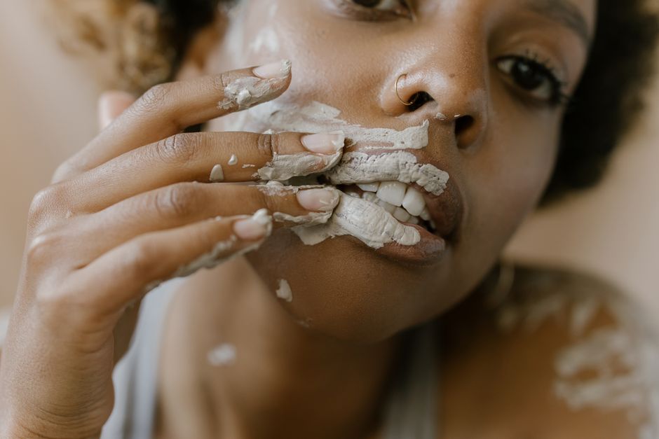 A woman applying a clay mask on her face in a close-up shot, emphasizing skincare.