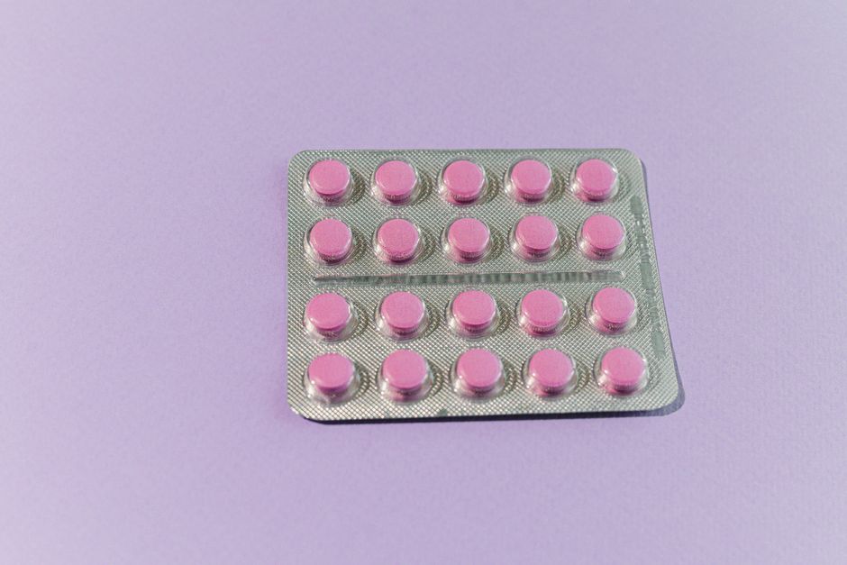 A neatly arranged blister pack containing pink tablets on a solid purple surface.