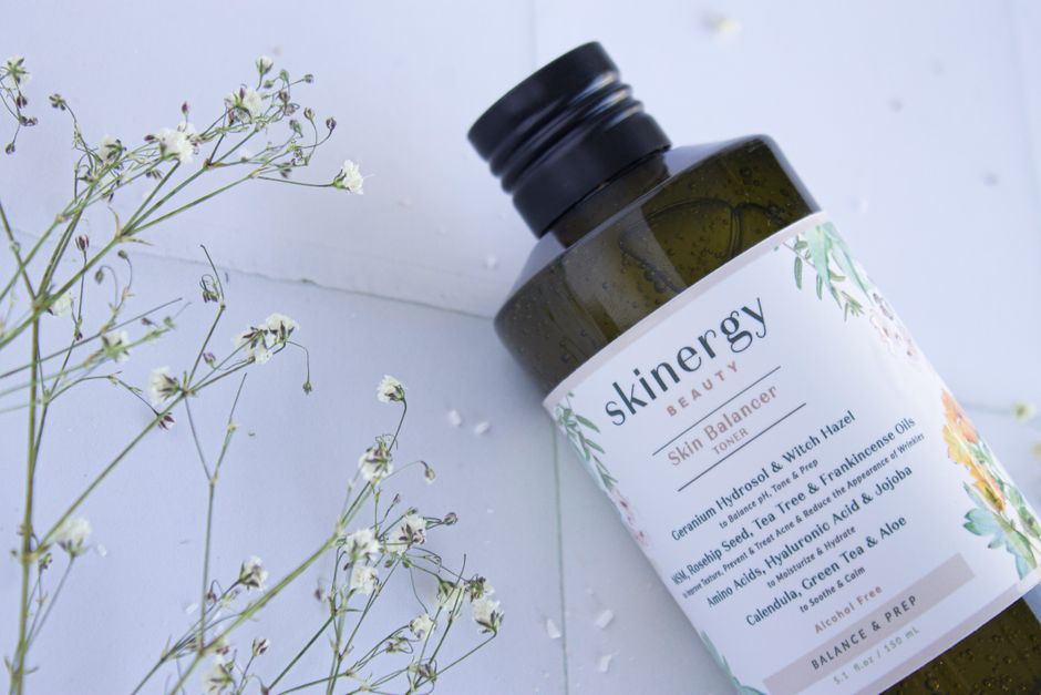 Close-up of a Skinergy toner bottle surrounded by delicate flowers, showcasing its natural essence.