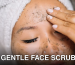 Woman with a head towel applying facial scrub for skincare routine.