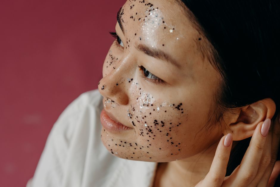 Close-up of a young Asian woman with a glittery face mask, smiling in a studio setting.