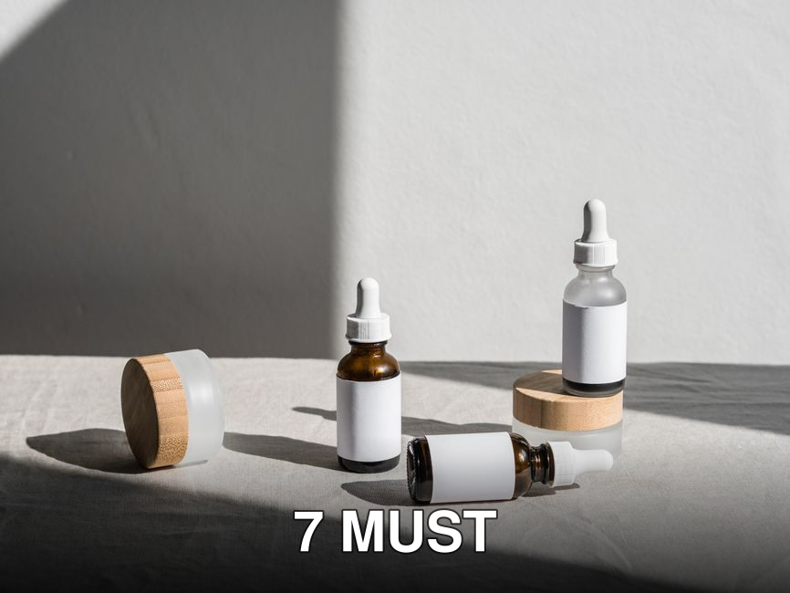 Minimalist composition of beauty bottles with droppers and containers on fabric under natural lighting.