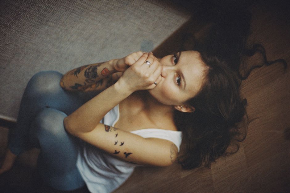 Vintage-style portrait of a tattooed woman sitting thoughtfully indoors.