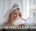 A woman with a towel on her head looking in a handheld mirror and smiling.