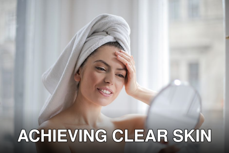 A woman with a towel on her head looking in a handheld mirror and smiling.