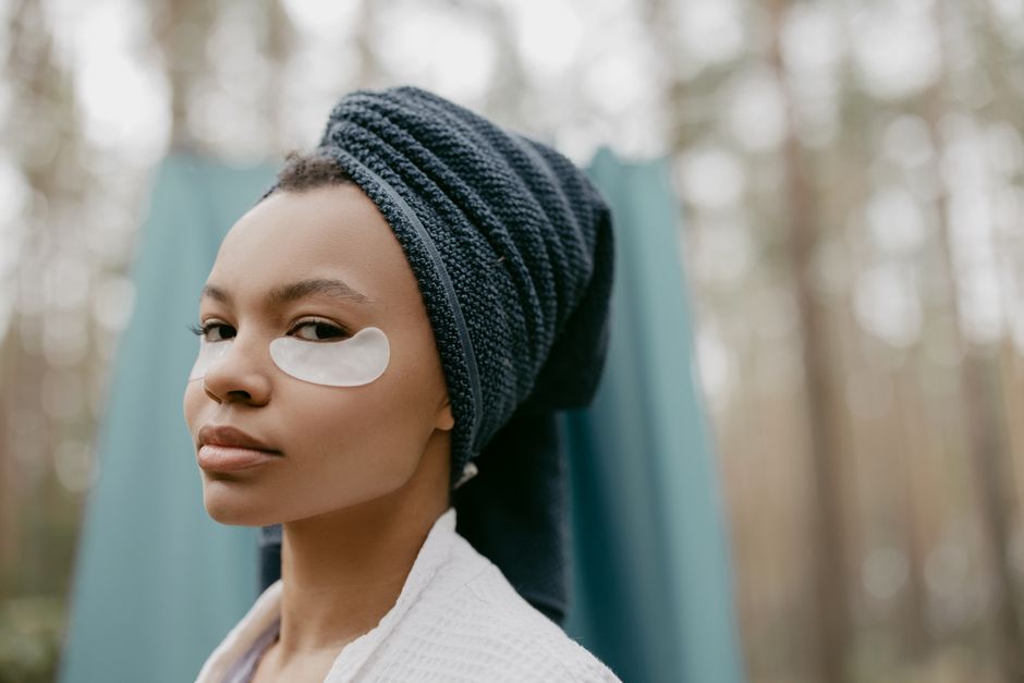 A serene portrait of a woman with eye patches and towel wrap, promoting self-care outdoors.