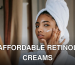 Young attentive ethnic female in bathrobe applying smear of moisturizing cream on face while looking in mirror at home