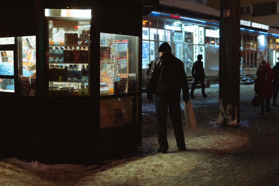 Man in black leather jacket stands outside shop at night in Saint Petersburg, Russia.