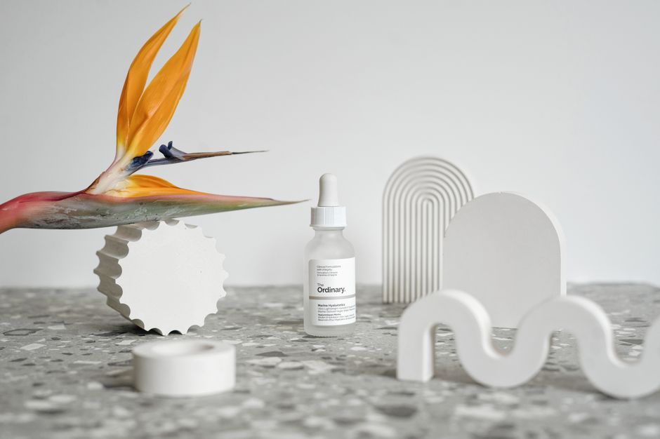 Modern still life featuring a cosmetic serum surrounded by abstract shapes and a Bird of Paradise flower.