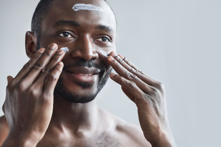 Smiling man applying face cream as part of his daily skincare routine for healthy skin.