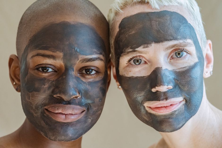 Crop positive diverse female friends with cosmetic masks on face looking at camera during spa procedures