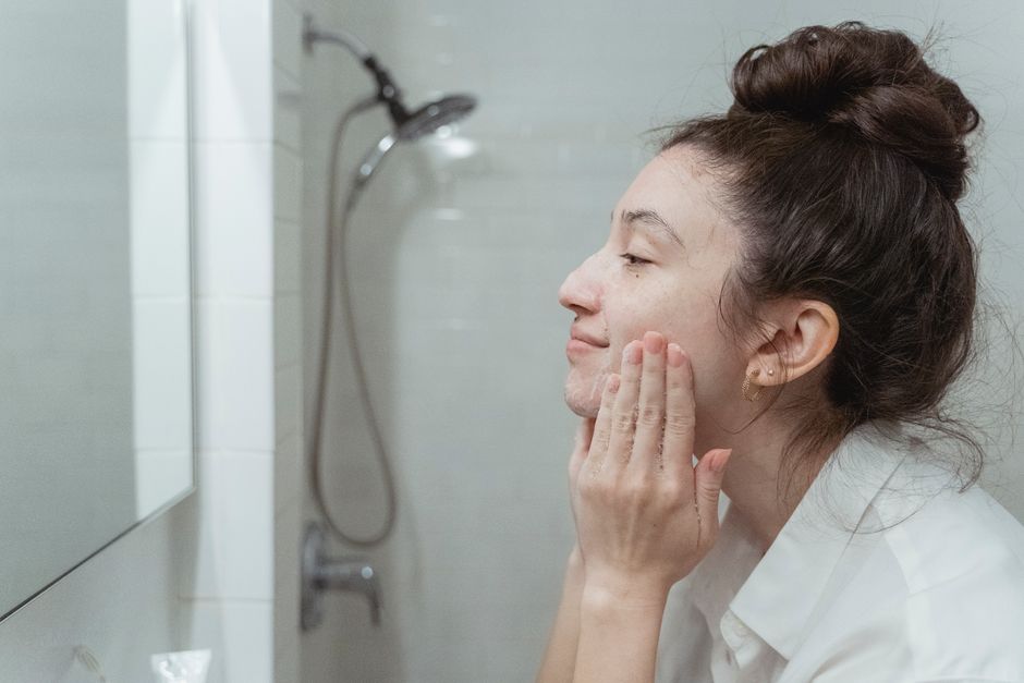A woman applying facial cream in a mirror for her skincare routine in a bathroom.