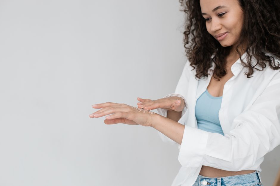 A woman gently applies exfoliating scrub to her hands, embodying a self-care routine.
