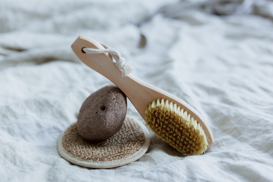 A natural bristle brush and pumice stone set against a soft, neutral fabric background.