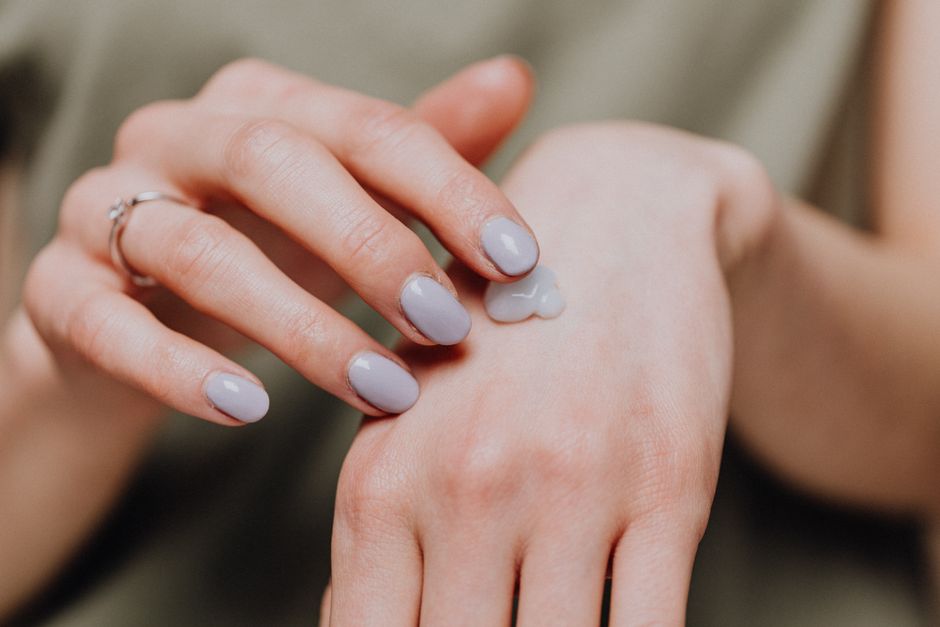 Crop unrecognizable female in casual shirt with trendy manicure and ring rubbing hand cream in back of hand skin