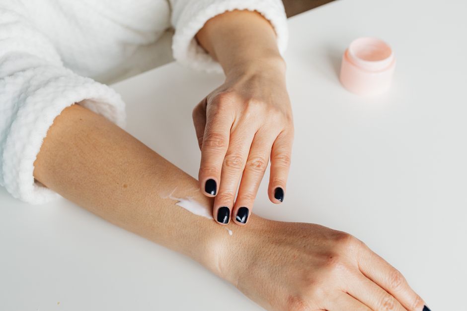 A woman applying moisturizer to her arm, showcasing skincare routine.