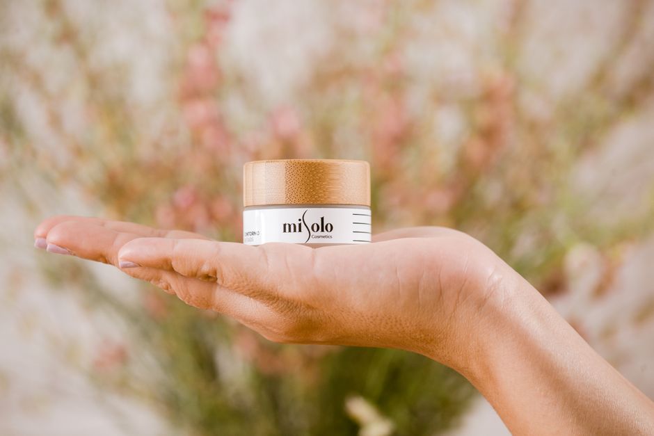Close-up of a woman's hand holding a Misolo cosmetics cream jar, set against a soft, blurred background.