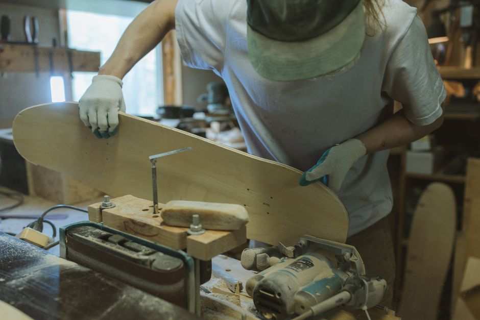 Artisan shaping a wooden skateboard in a workshop with precision tools.