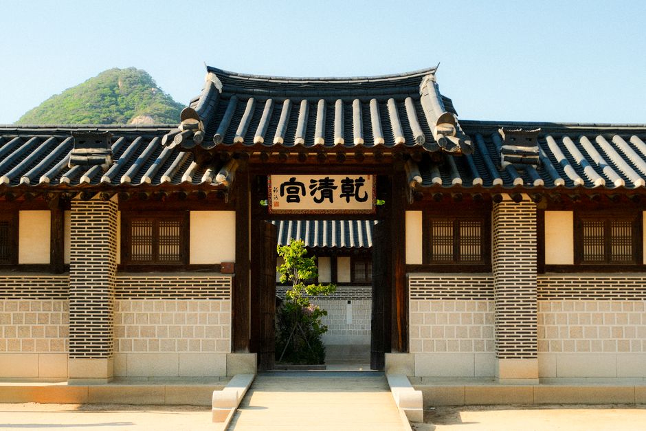 A scenic view of a traditional Korean building with a mountain backdrop under a clear blue sky.