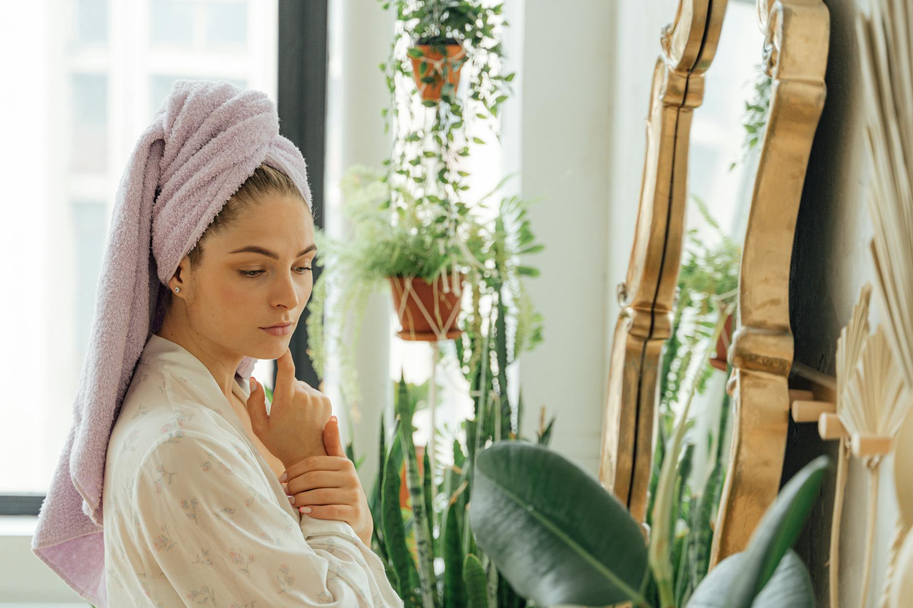 Beautiful woman with towel on her head surrounded by plants, reflecting in a mirror.