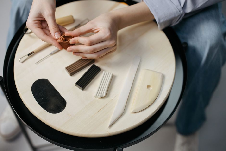 Close-up of hands crafting clay art with tools on a wooden board, showcasing creativity and precision.
