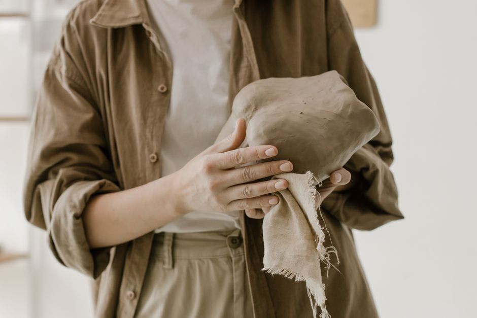 Person molding clay with hands in a calm, earthy setting, showcasing pottery craftsmanship.