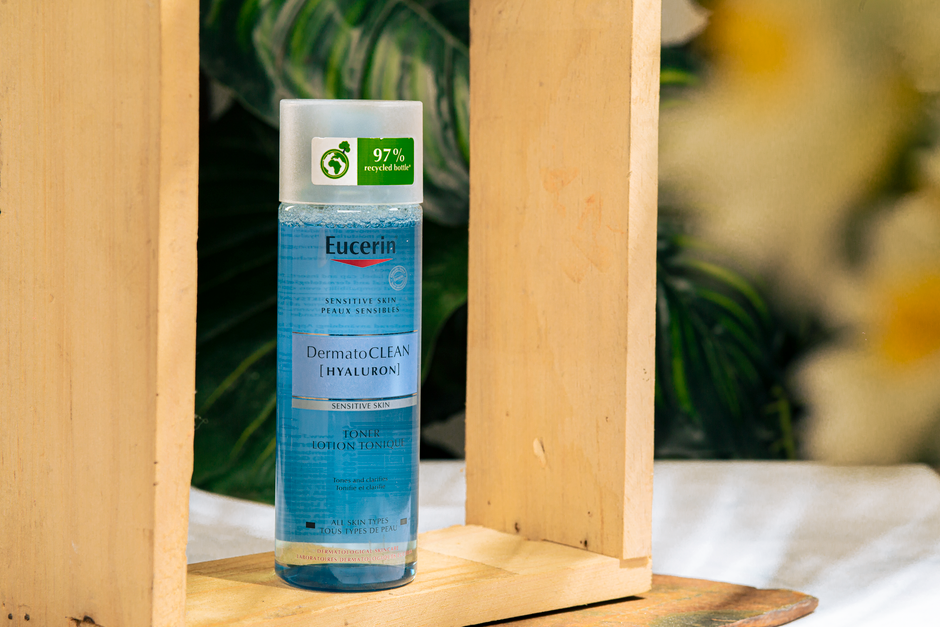 Eucerin DermatoCLEAN Hyaluron toner bottle surrounded by wooden frame and plants.