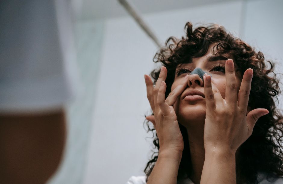From below of young curly brunette standing in front of mirror and cleansing nose skin with cosmetic strip