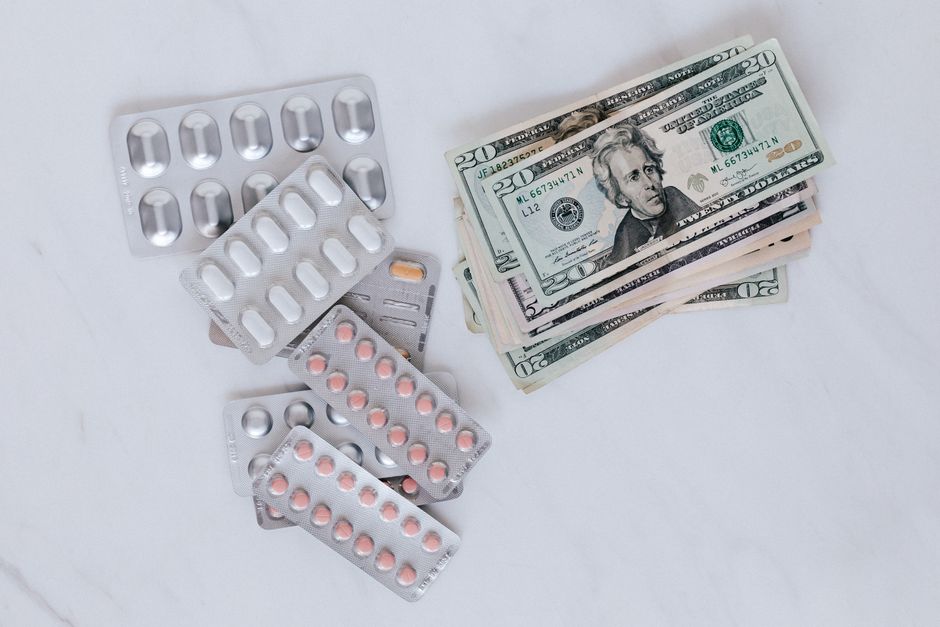 From above of silver blister full of drug near big pile of dollar to spend on medication
