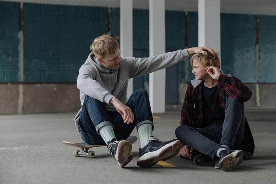 Two teenagers enjoy skateboarding and bonding in an indoor space, showcasing friendship and leisure.