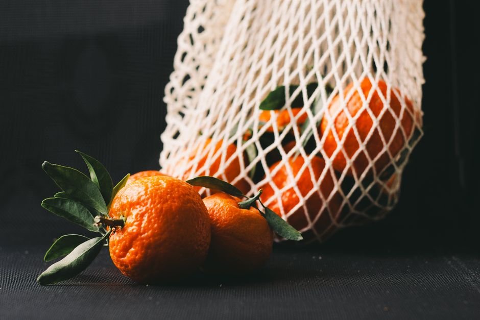 Vibrant tangerines in a reusable mesh bag on a dark background.