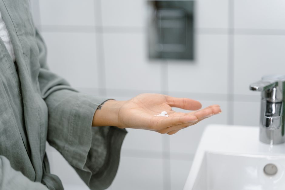 A close-up of a hand holding cream near a modern bathroom sink.