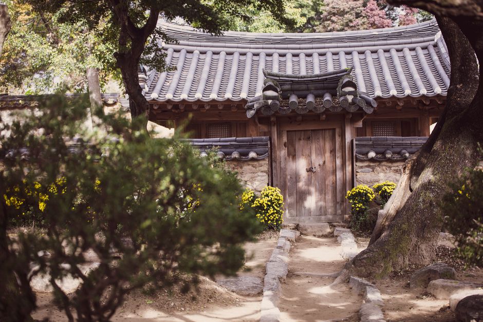 Charming traditional Korean house surrounded by a serene garden setting with vibrant flowers and lush trees.