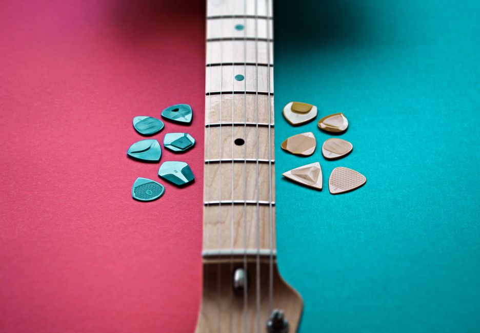 Close-up of an electric guitar neck with assorted picks on a vibrant red and teal background.