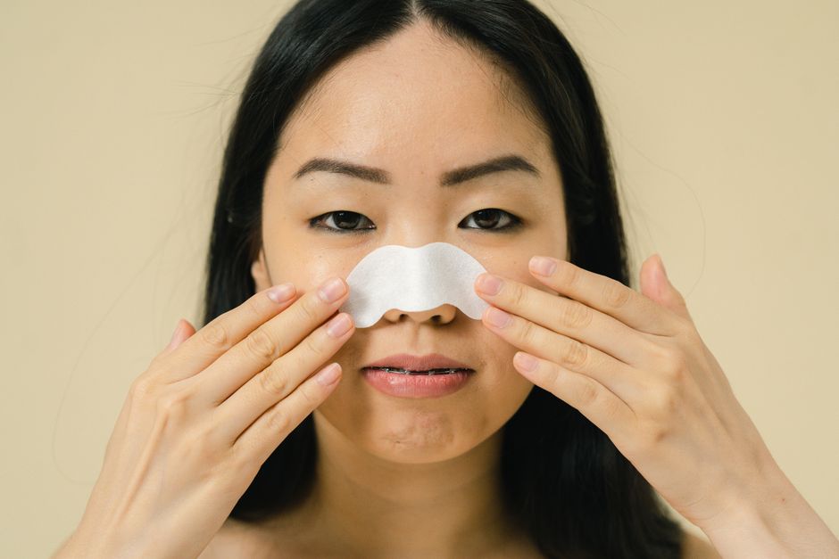 Close-up portrait of a woman using a nose strip for skin care treatment in a studio setting.