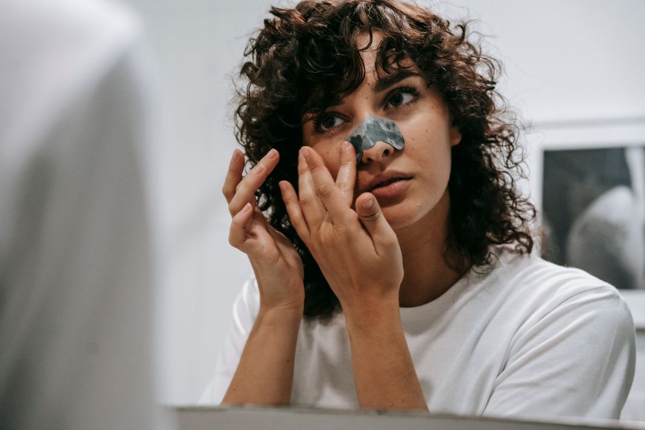 Young female in white t shirt applying blackhead strip on nose standing in front of mirror