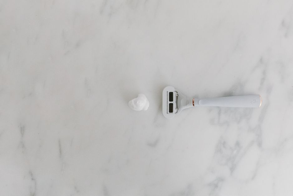 A minimalist scene with a shaving razor and foam on a marble background, offering copyspace.