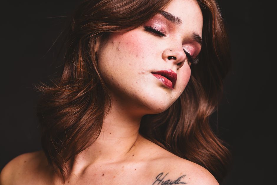 Close-up portrait of a woman with eyes closed, showcasing makeup and tattoo.