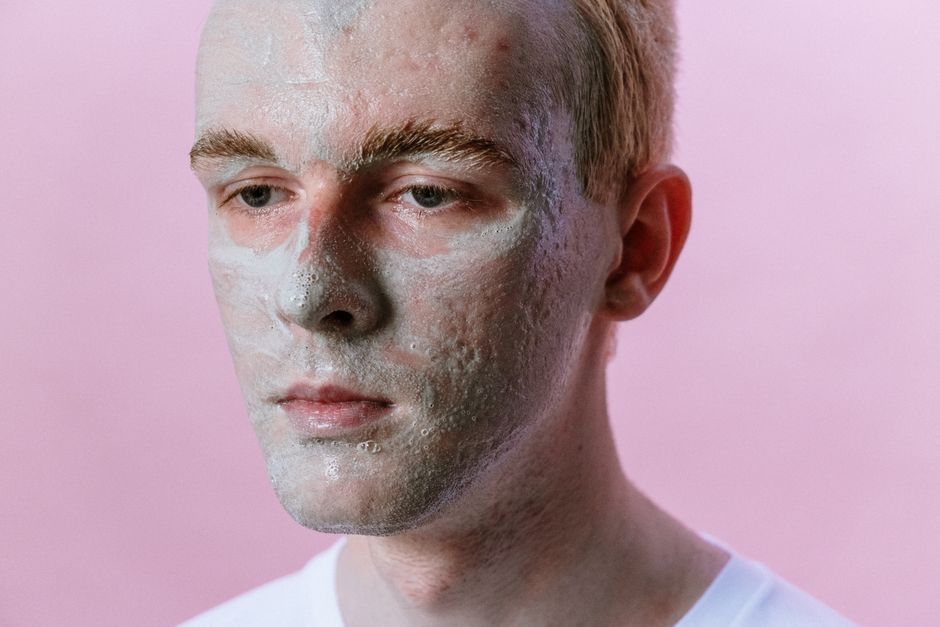 Portrait of a young man with a clay face mask against a pink background, highlighting skincare and beauty routines.