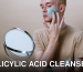 Young man applying clay mask for skincare routine indoors with a mirror.