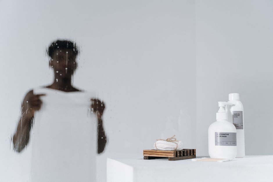 Blurred reflection of a man with skincare bottles on a white background.