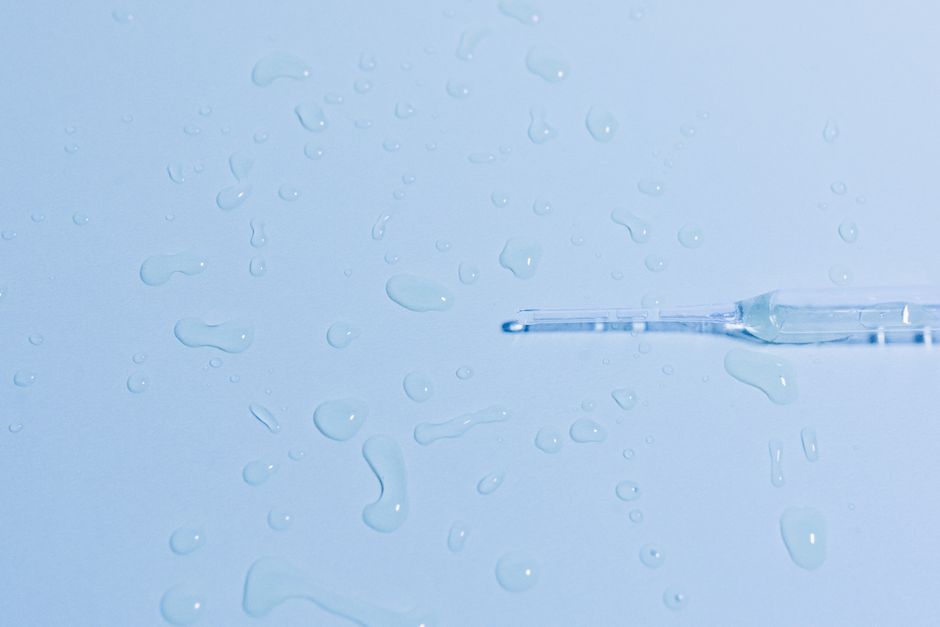 Detailed close-up of a glass pipette on a wet surface with scattered water droplets.