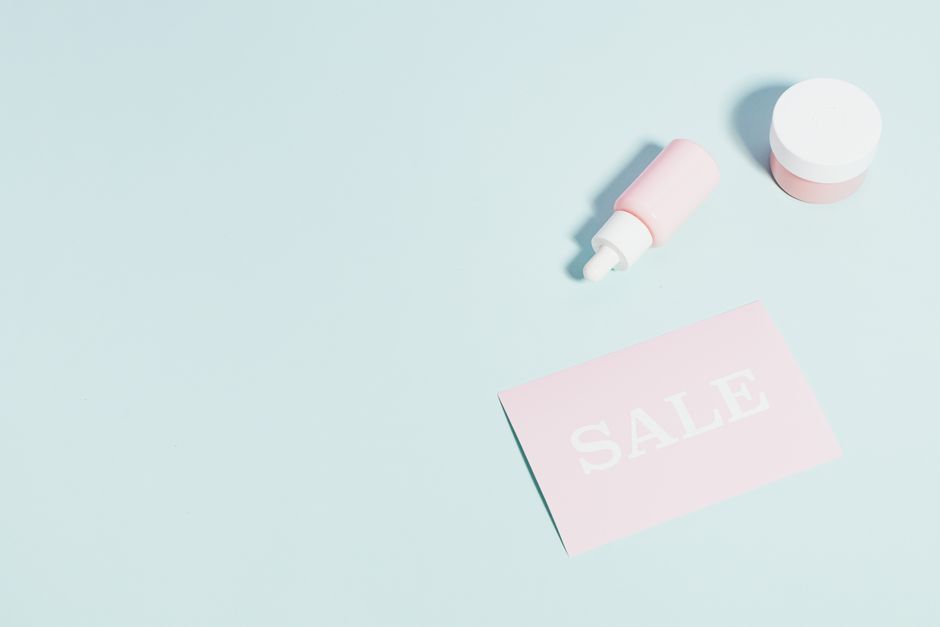 Pink beauty products and sale sign on pastel backdrop.