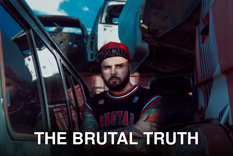 Man with tattoos and red cap in an urban junkyard, showcasing industrial style.