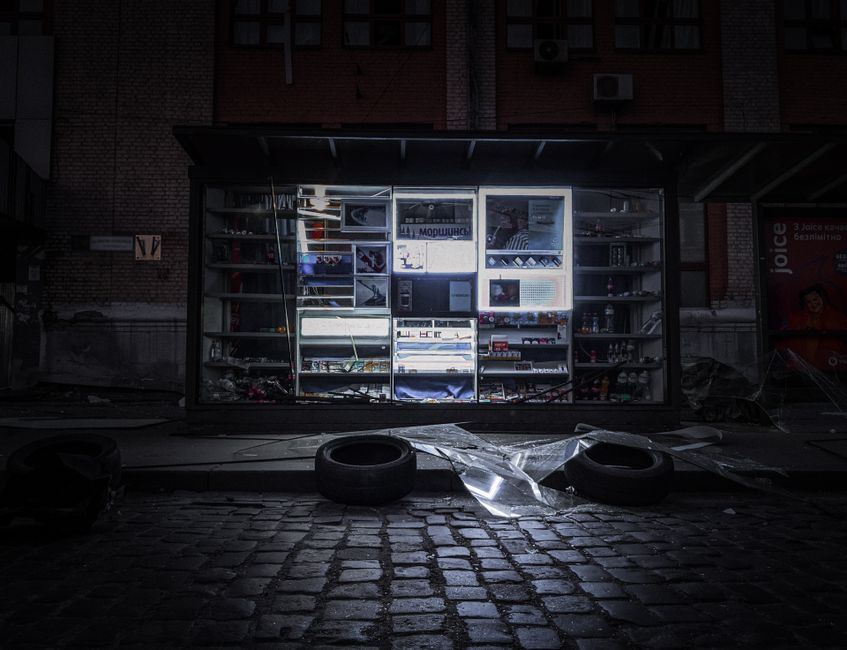 A shopfront in Kyiv illuminated at night, showcasing products amidst cobblestone pavements.