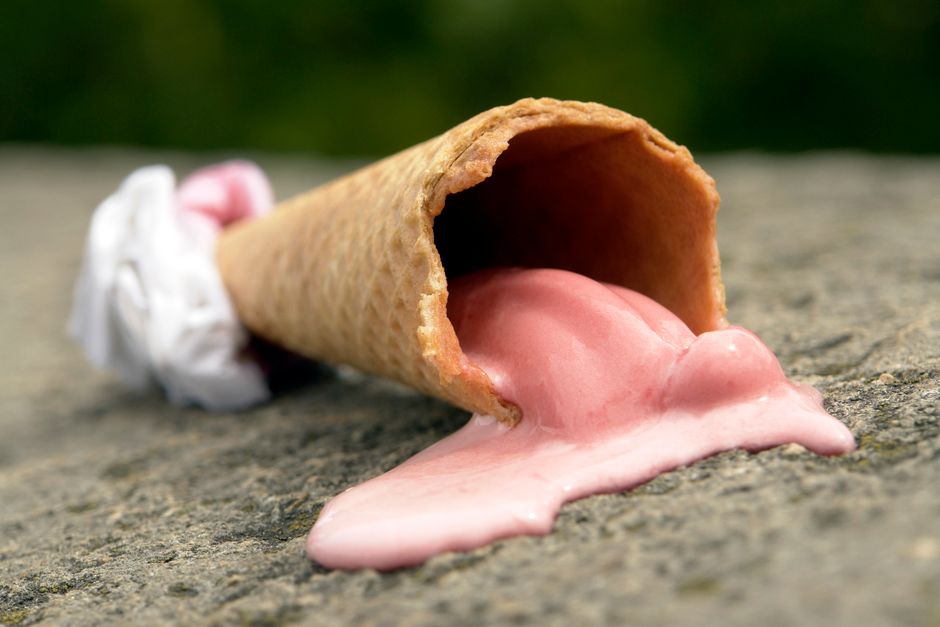 A melting strawberry ice cream cone lies on a stone surface, highlighting summer's heat.