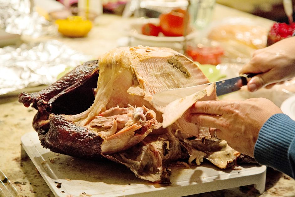 Close-up of hands slicing a roasted turkey on a kitchen counter, capturing the essence of a Thanksgiving feast.