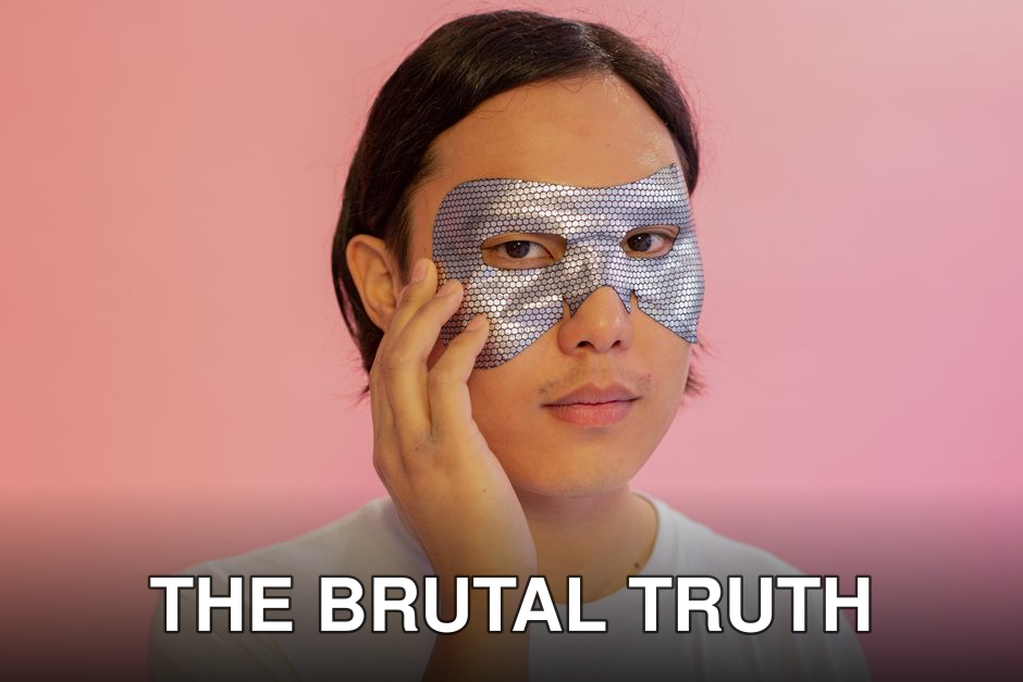 Emotionless young Asian male in white shirt with cosmetic eye mask touching face and looking at camera against pink background